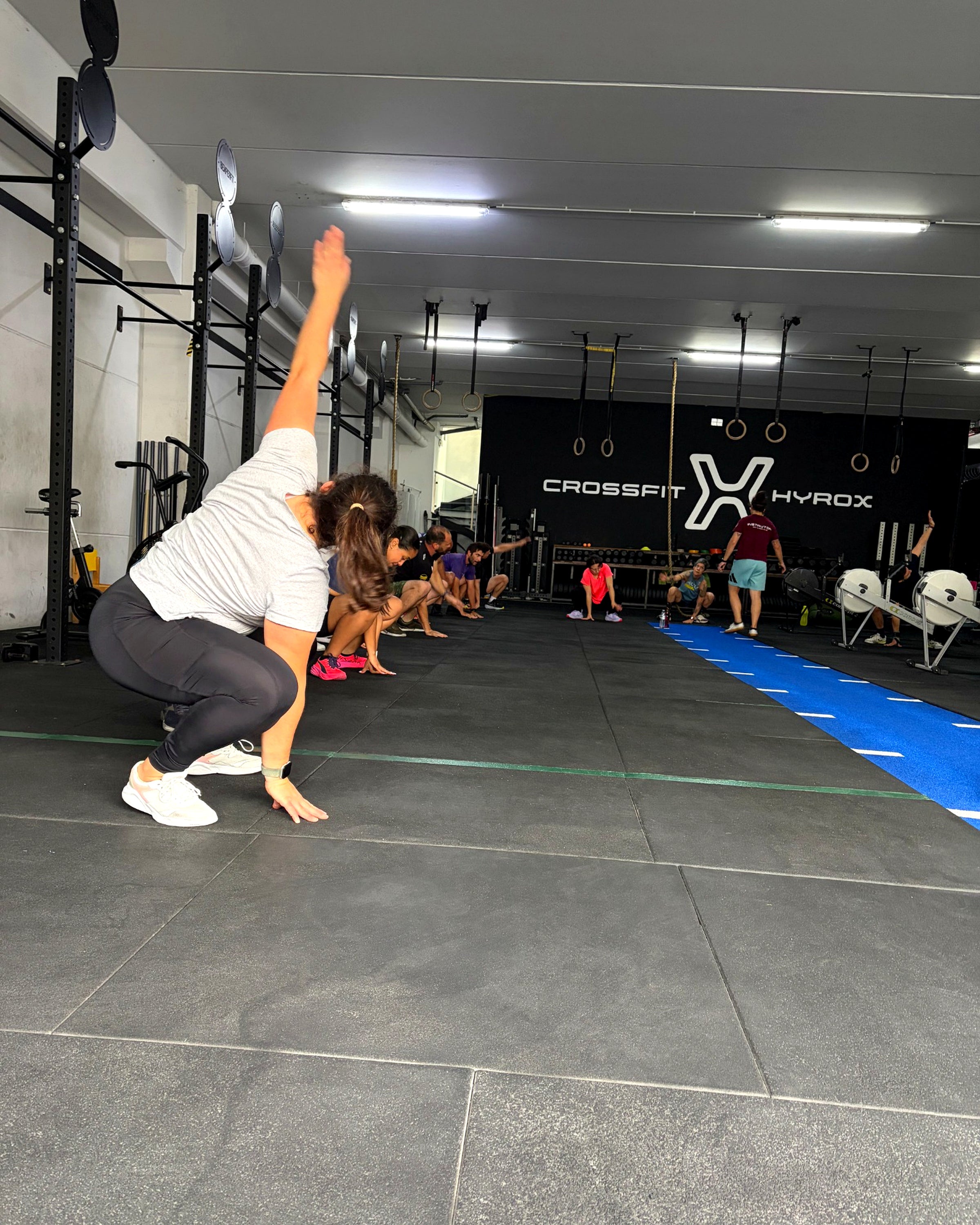 Aula de grupo na box do Higia Training Club, com atletas em treino e referências às modalidades CrossFit e Hyrox ao fundo.